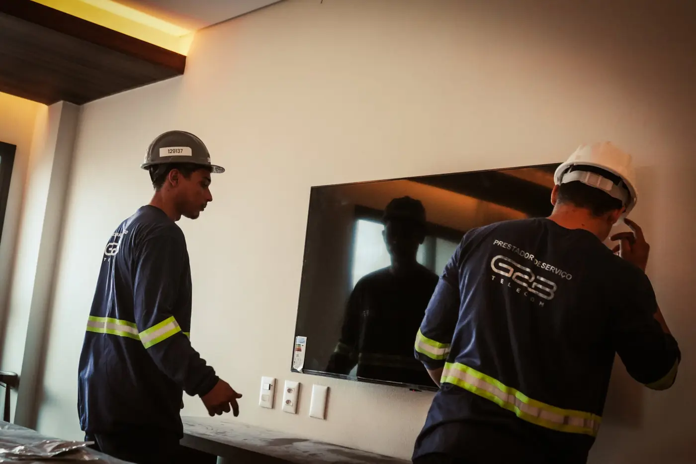 Técnicos da G2B com capacete e uniforme refletivo instalando equipamento